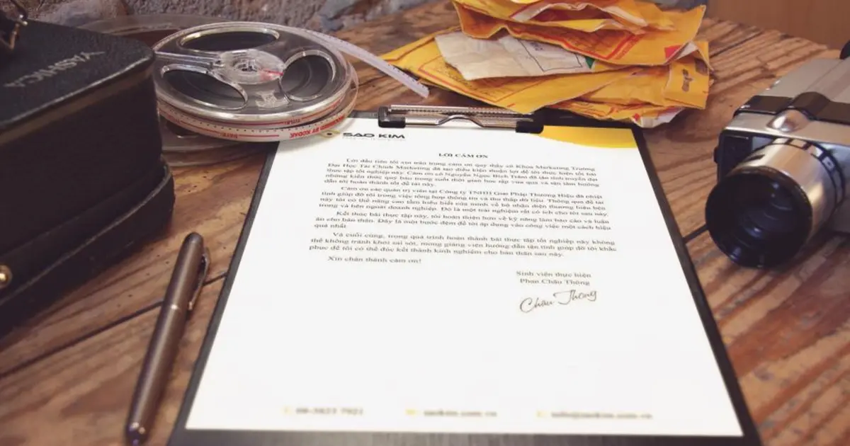 Prancheta com documento, caneta e envelopes sobre mesa de madeira